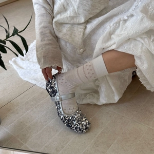 Close-up of silver sequin Mary Jane shoes with buckle and lace socks on model