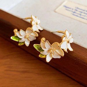 Detail of enamel gardenia flower earrings with green leaves on a wooden stand