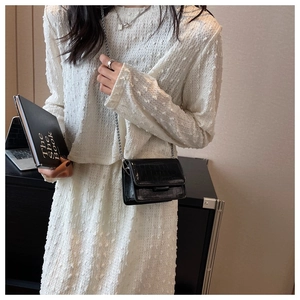Detail of black crocodile texture mini bag with silver chain worn by a model in a dress
