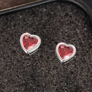 Macro shot of silver heart studs featuring faceted red zircon on a black textured background