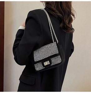 Detail of a black rhinestone crossbody bag with a silver chain and metal turn-lock closure