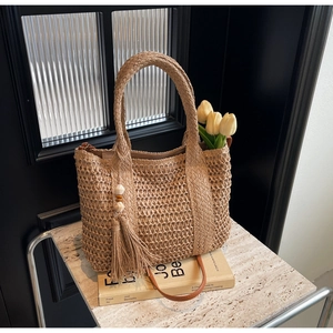 Close-up of beige woven straw tote bag featuring decorative tassels and wooden beads