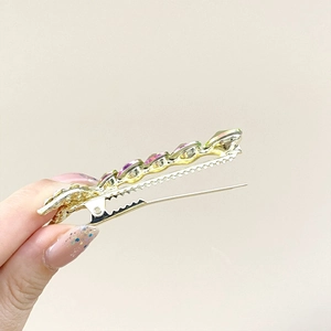 Detail of gold metal mermaid tail clip featuring pink and green crystal rhinestones