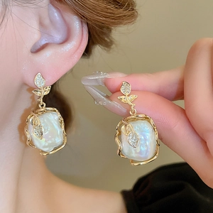 Détail des boucles d'oreilles fleur en perle baroque avec feuilles dorées et cristaux