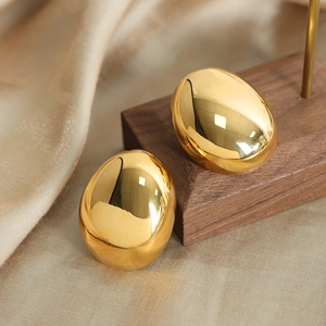 Polished gold egg-shaped oval stud earrings on walnut wood and beige silk background
