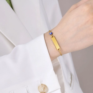 Detail of a gold stainless steel bracelet with custom engraving plate and evil eye charm