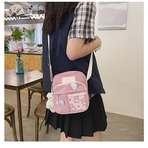Détail d'un sac bandoulière rose en toile avec broderies cartoon et pendentif peluche