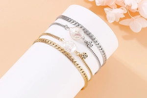 Detail of layered gold and silver bracelets featuring baroque pearls and flower pendants