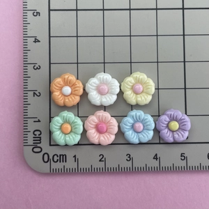 Mini glossy resin flower charms in assorted colors on a measurement grid for DIY nail art