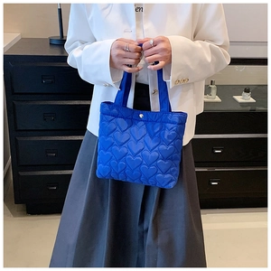 Detail of blue heart-quilted nylon tote bag showing texture and stitching on the handle