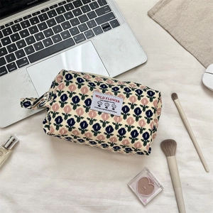 Detailed close-up of a floral corduroy cosmetic bag on a desk with a laptop and makeup