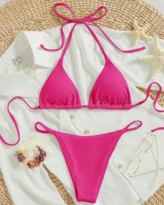 Flat lay of ribbed fuchsia halter bikini with summer beach accessories on a straw mat