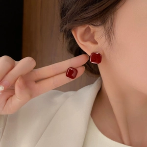 Macro detail of red geometric stud earrings with gold trim and glossy resin finish
