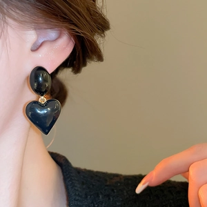 Close-up of black oval and heart earrings on model ear with gold metallic edges