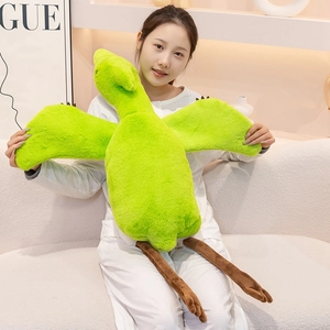 A soft green cartoon pterosaur plush pillow toy held by a smiling woman on a white sofa