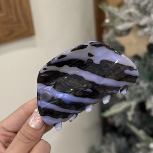 Close-up of a large hair claw clip with black and purple swirl texture held by hand
