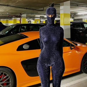 Détail d'une combinaison à strass bleus avec masque devant une voiture de sport orange