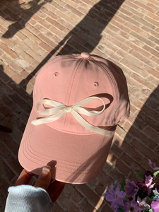 Close-up of pink baseball cap featuring a delicate white satin bow detail on the front