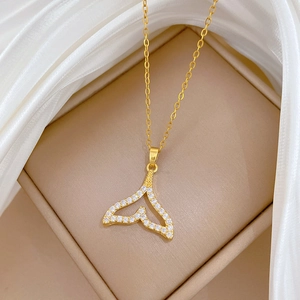 Close-up of golden fishtail pendant with sparkling zircons on white silk background