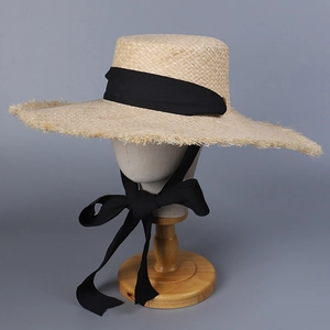 Close-up of wide-brim raffia sun hat with raw edges and elegant black ribbon ties