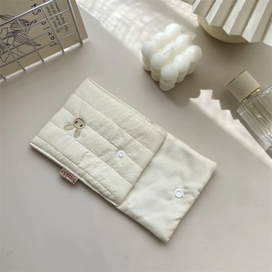 Detail of cream quilted makeup bag featuring cute rabbit embroidery and button closure