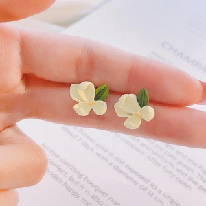 Close-up of small tulip flower stud earrings with green leaves held between fingers