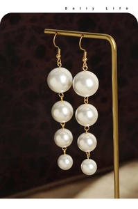 Detailed view of long white faux pearl tassel earrings with golden hooks on a stand