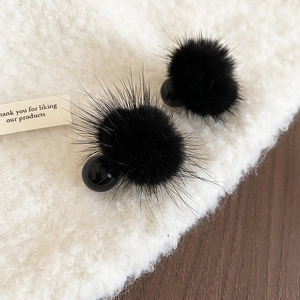 Gros plan de boucles d'oreilles pompons noirs avec perles brillantes sur tissu beige