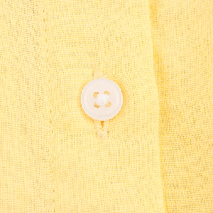 Detail of white button and yellow cotton linen fabric texture on stylish summer shirt