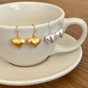 Macro detail of brushed heart earrings in gold and silver on a white ceramic cup