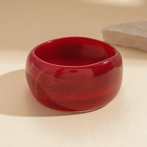 Close-up of a glossy red acrylic resin bangle on a beige background with textured stone