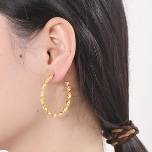 Close-up of golden twisted hoop earring with wavy texture worn by a model