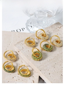 Detailed shot of gold-plated geometric hoop earrings with white and emerald green stones