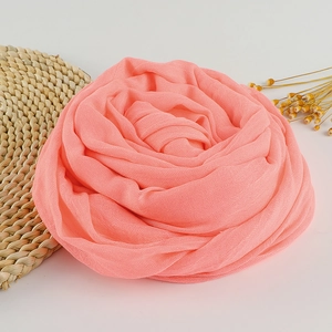 Coral pink linen cotton scarf folded into a rose shape on a rustic woven mat with yellow flowers