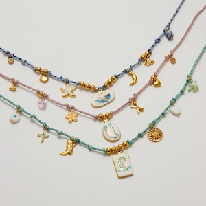Flat lay of colorful 18K gold necklaces with enamel charms like heart, moon, and flowers
