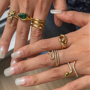 Close-up of gold snake rings set with green teardrop gemstone and crystal accents