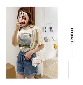 Close-up of cream plaid crossbody bag paired with a scenic graphic tee and chain strap