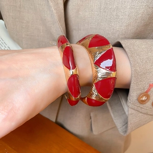 Detail of red enamel and gold open bangles styled with a beige blazer for a retro look