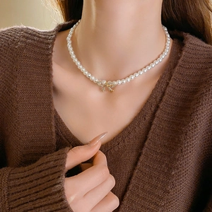 Détail macro d'un collier de perles avec pendentif nœud doré orné de strass étincelants