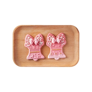 Pink Christmas bell cookie molds with bow and snowflake patterns on a wooden tray