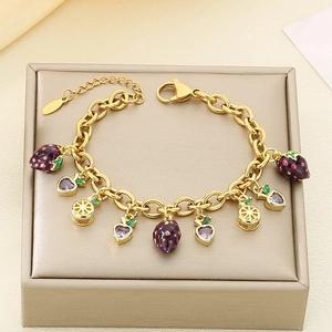 Detailed shot of a gold charm bracelet with purple strawberry and orange slice pendants