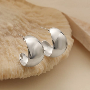 Vue détaillée de boucles d'oreilles argentées en forme de C sur un fond de corail