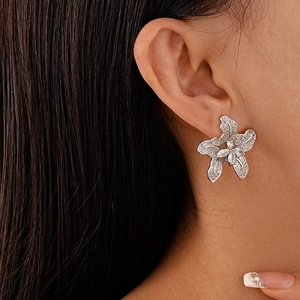 Close-up of sparkling zircon flower earrings with silver studs on a female model