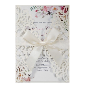 Macro detail of ivory laser-cut wedding invitation with glitter finish and satin bow