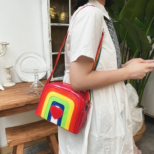 Close-up of a red rainbow crossbody bag with heart detail and woven shoulder strap
