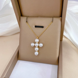 Detail of a gold titanium steel cross necklace with pearls in a brown leather gift box