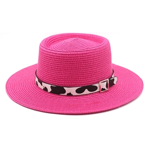 Detail of bright pink straw boater hat featuring a cow print ribbon and silver buckle