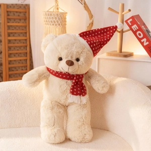 Teddybär mit roter Weihnachtsmütze und Schal auf einem gemütlichen weißen Sofa