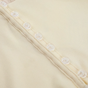 Detailed close-up of cream ribbed knit fabric with transparent buttons on long sleeve top