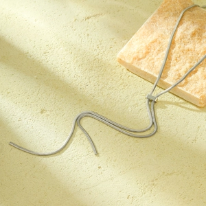 Minimalist silver double-strand snake chain necklace on a sandy textured background